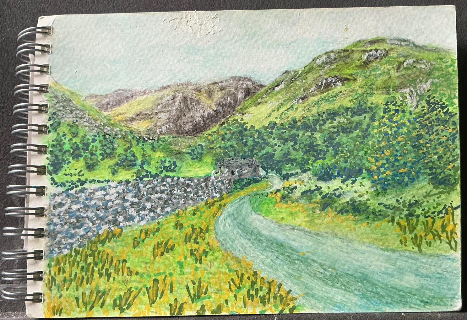 My first attempt using the postcard sized art pad and watercolour pencils, with some acrylic pens as well. It’s somewhere in the Lake District. My mind was in a haze at the time so I can’t remember where.